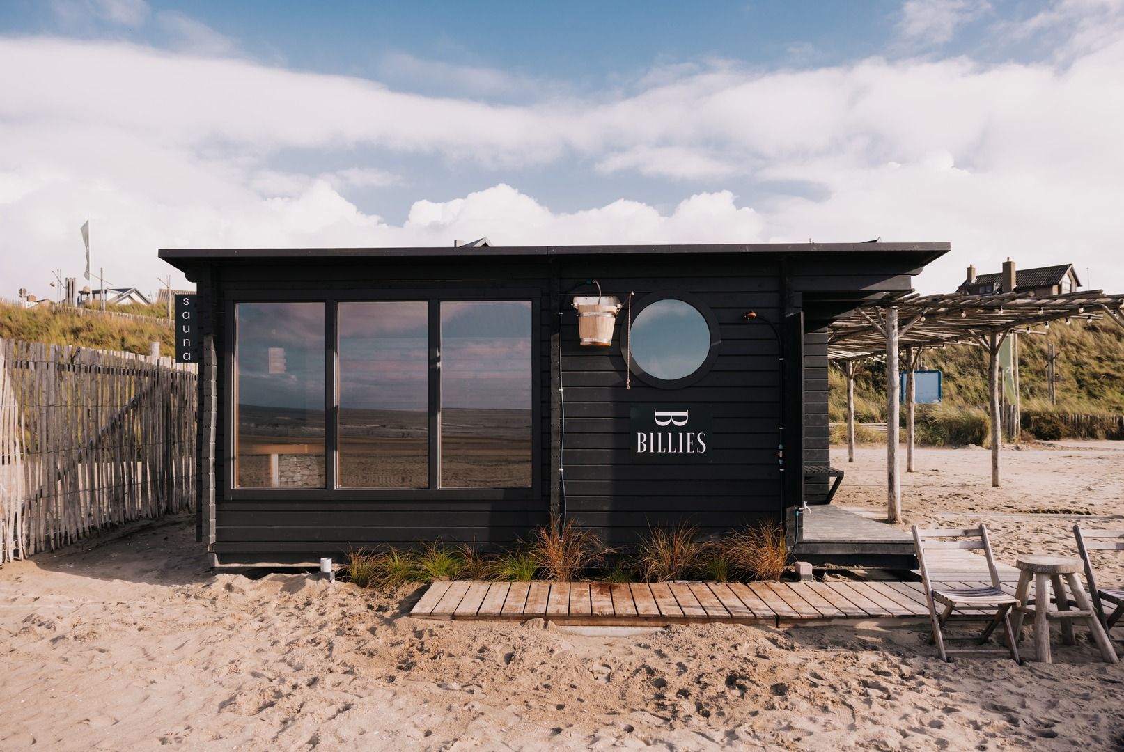 De zwarte houten sauna van Billies met een rond raam, op het zand in Zandvoort