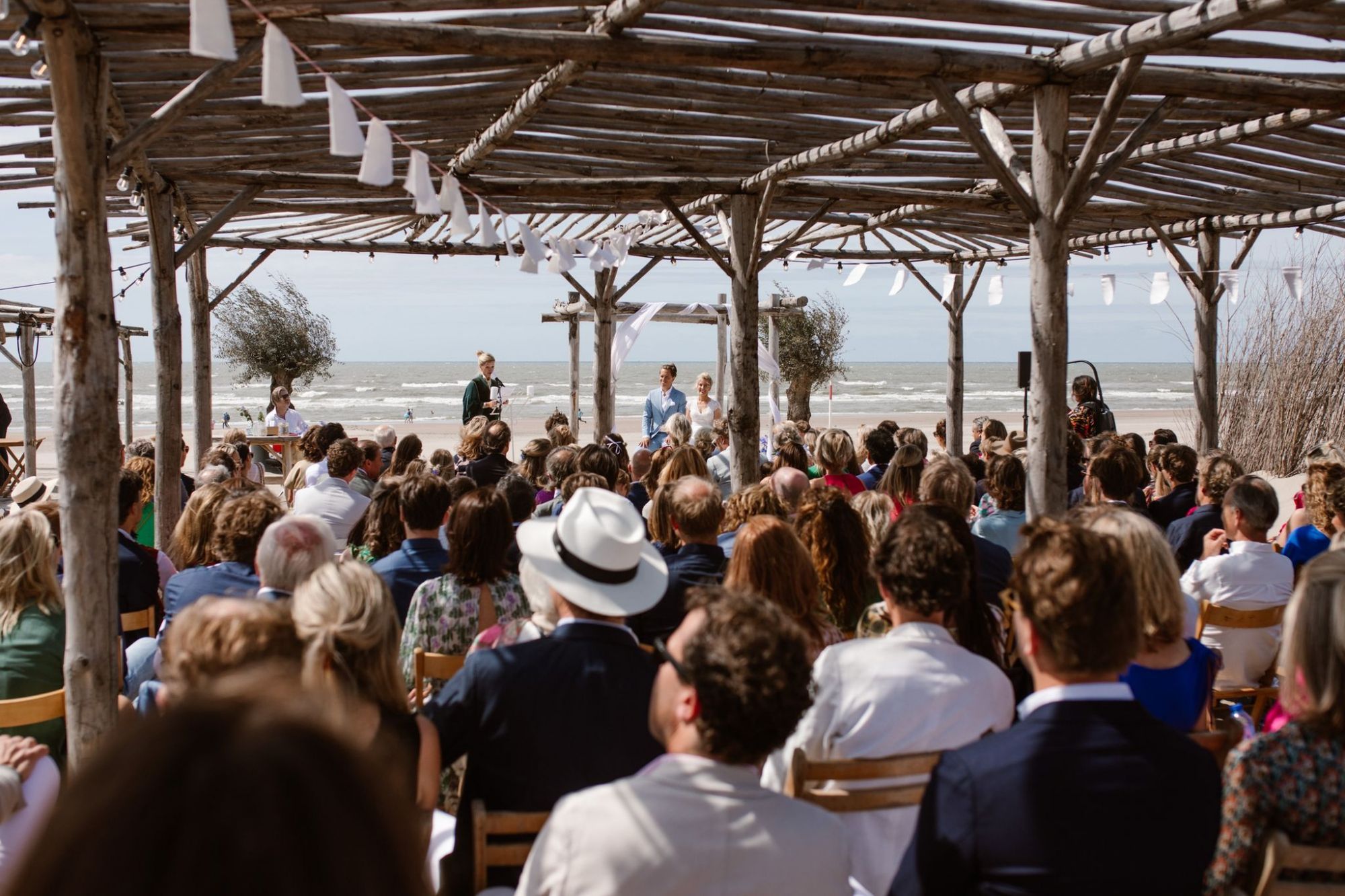 Gasten onder de houten pergola tijdens een trouwceremonie op het strand